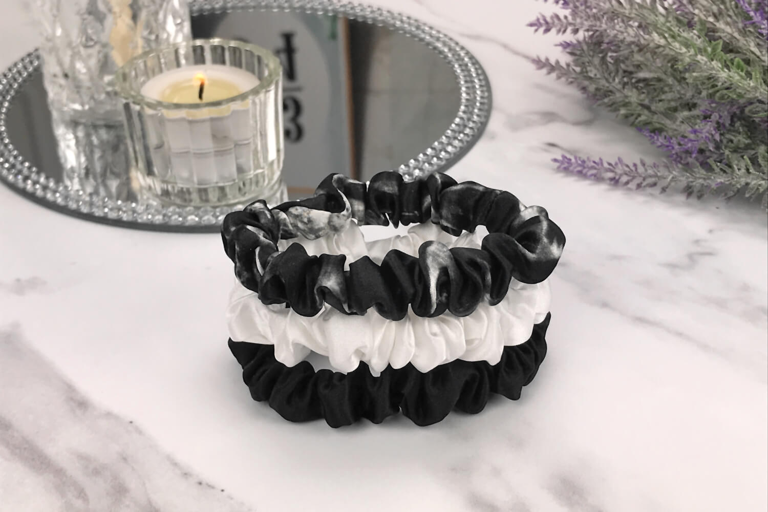 Celestial Silk skinny black marble black and ivory silk scrunchies stacked on marble counter with lavender plant and a candle in the background