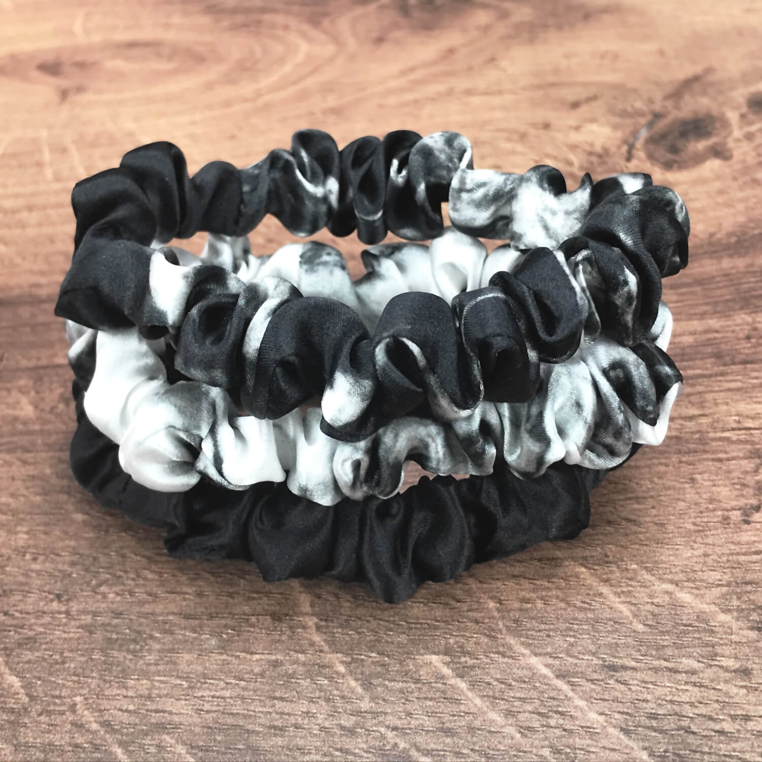 thin white marble black marble and black silk hair ties by Celestial Silk stacked in a pile on a wood vanity