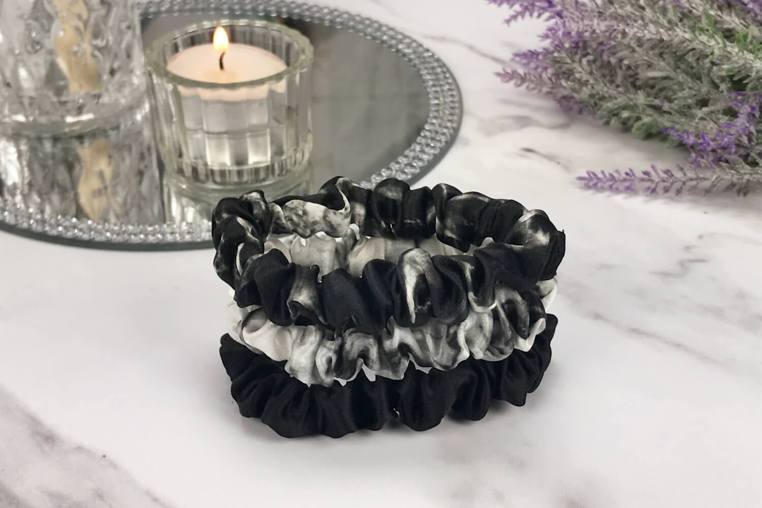 Celestial Silk skinny white marble black marble and black silk scrunchies stacked on marble counter with lavender plant and a candle in the background