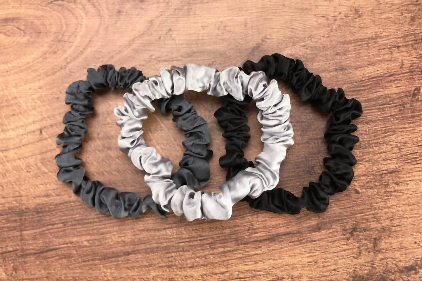 thin charcoal black and silver silk hair ties by Celestial Silk laying in a pile on a wood vanity