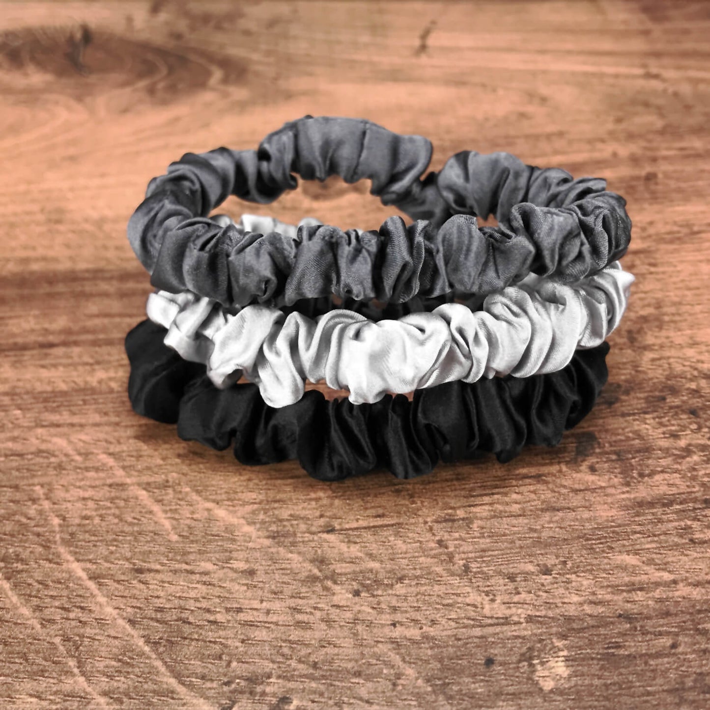 thin charcoal black and silver silk hair ties by Celestial Silk stacked in a pile on a wood vanity