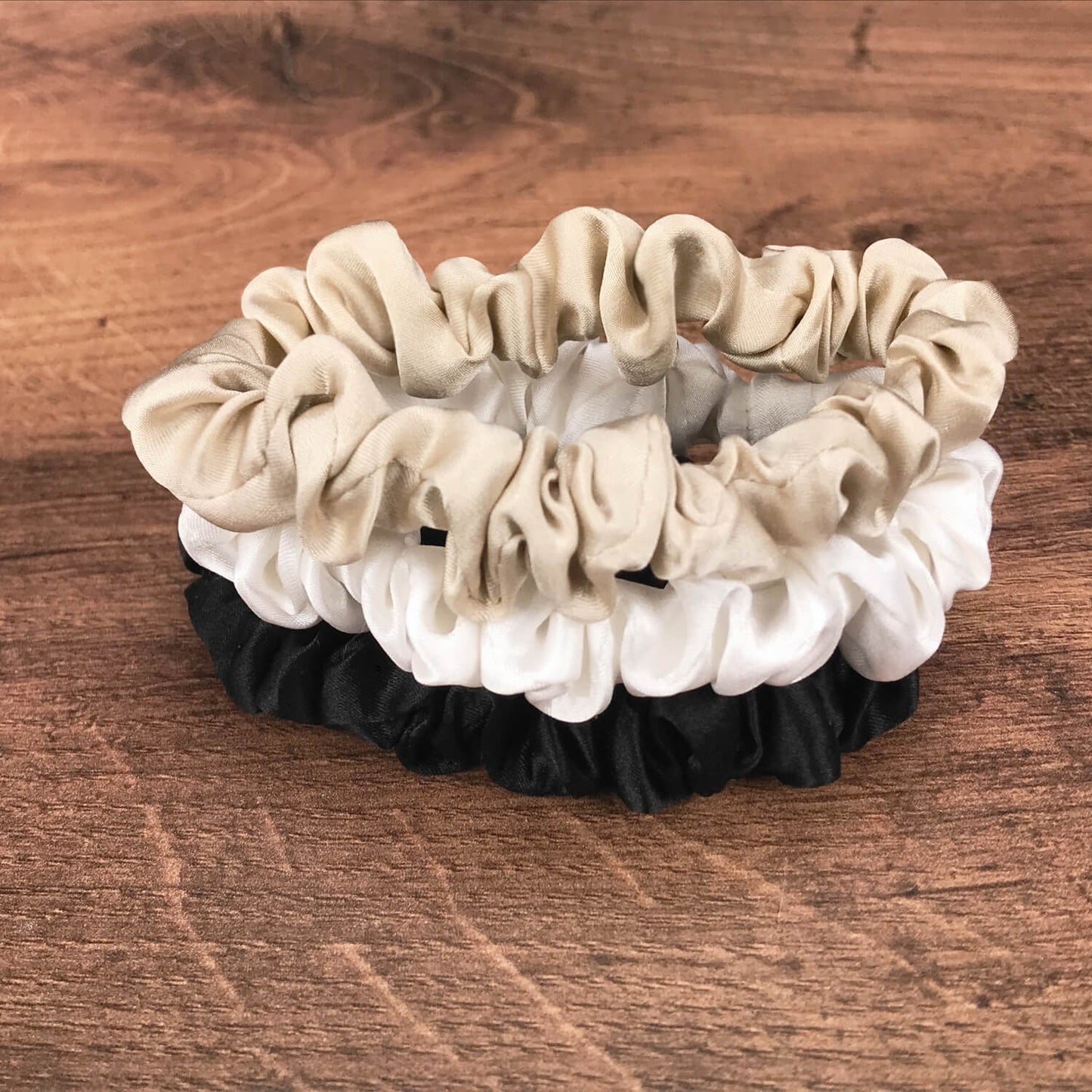 thin taupe ivory and black silk hair ties by Celestial Silk stacked in a pile on a wood vanity