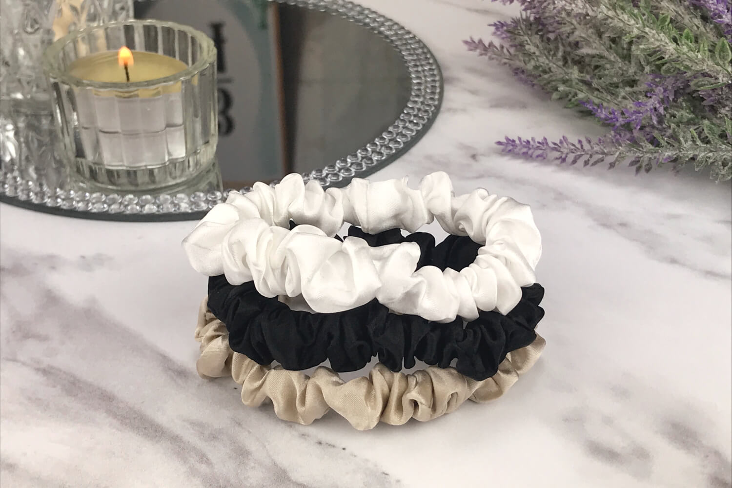 Celestial Silk skinny taupe ivory and black silk scrunchies stacked on marble counter with lavender plant and a candle in the background