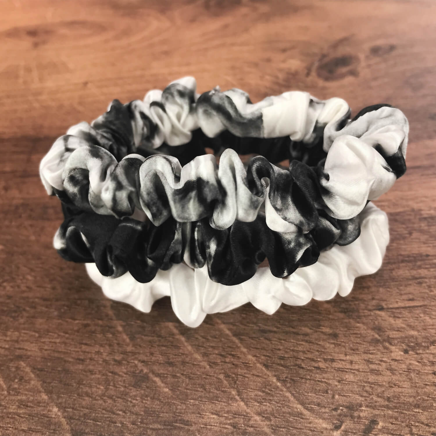 thin white marble ivory black marble silk hair ties by Celestial Silk stacked in a pile on a wood vanity