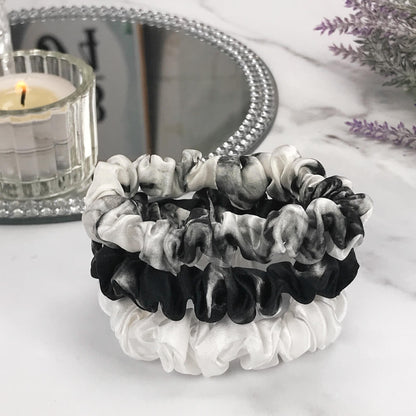Celestial Silk skinny white marble ivory black marble silk scrunchies stacked on marble counter with lavender plant and a candle in the background