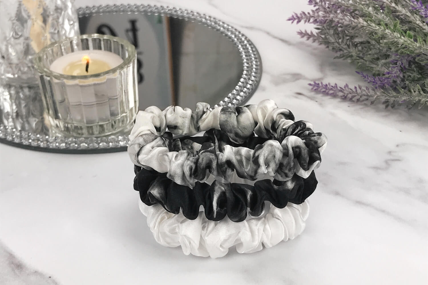 Celestial Silk skinny white marble ivory black marble silk scrunchies stacked on marble counter with lavender plant and a candle in the background