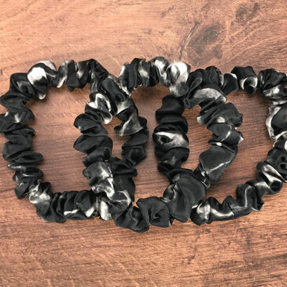 thin black marble silk hair ties by Celestial Silk laying in a pile on a wood vanity