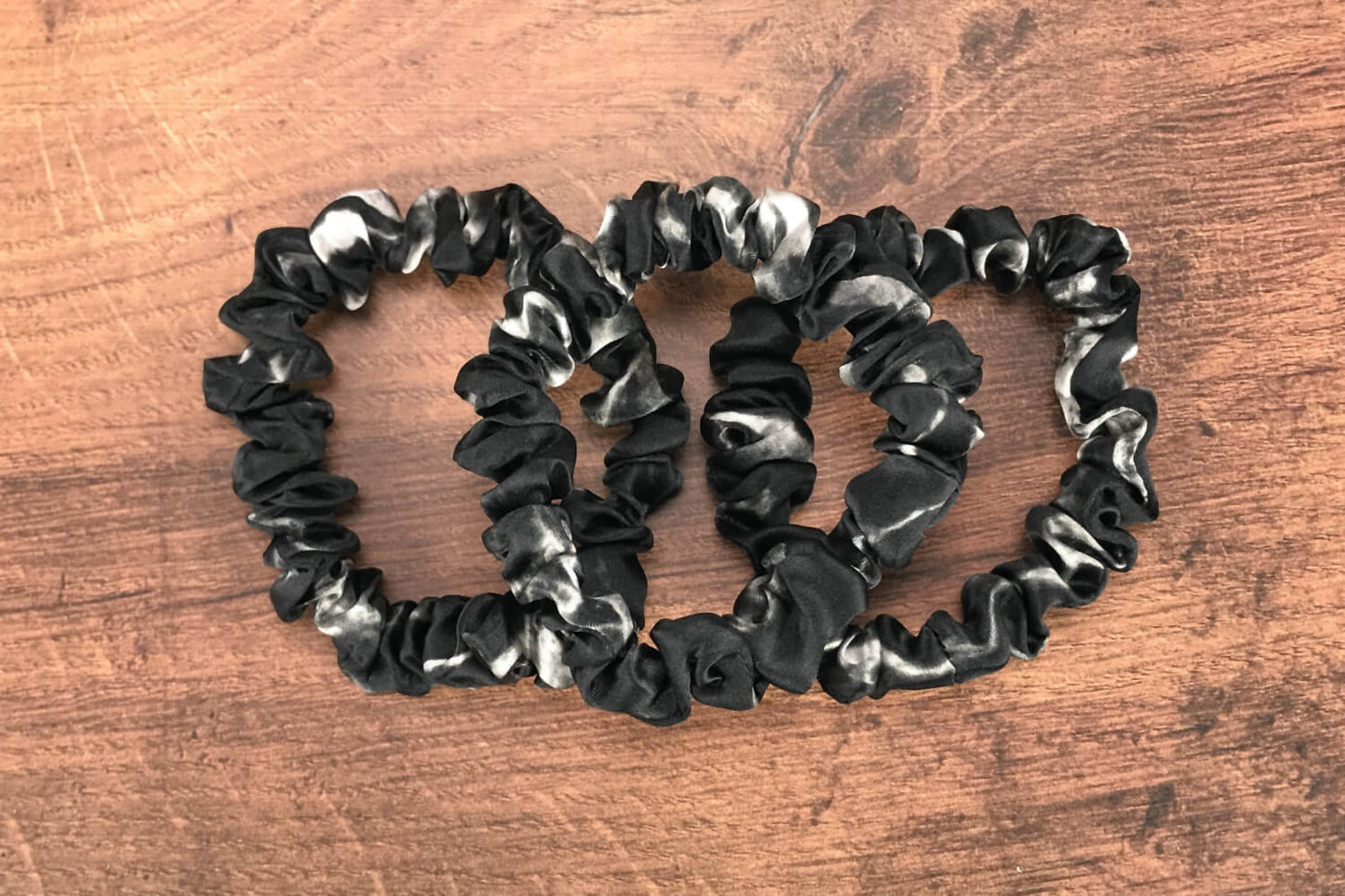thin black marble silk hair ties by Celestial Silk laying in a pile on a wood vanity