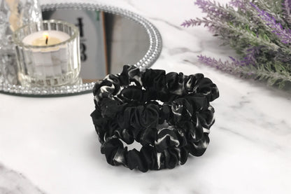 Celestial Silk skinny black marble silk scrunchies stacked on marble counter with lavender plant and a candle in the background