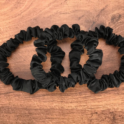 thin black silk hair ties by Celestial Silk laying in a pile on a wood vanity