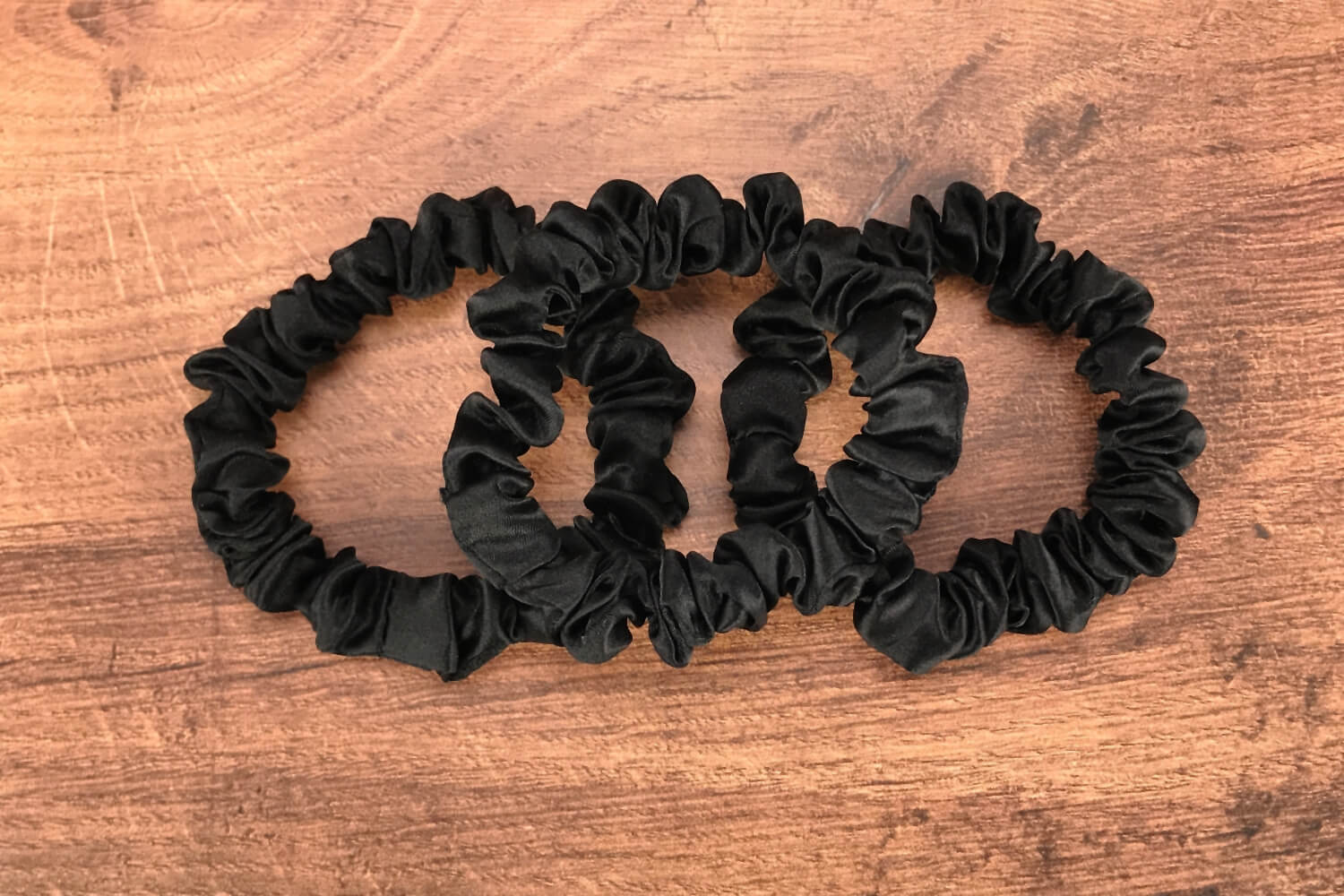 thin black silk hair ties by Celestial Silk laying in a pile on a wood vanity