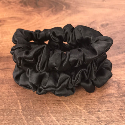 thin black silk hair ties by Celestial Silk stacked in a pile on a wood vanity