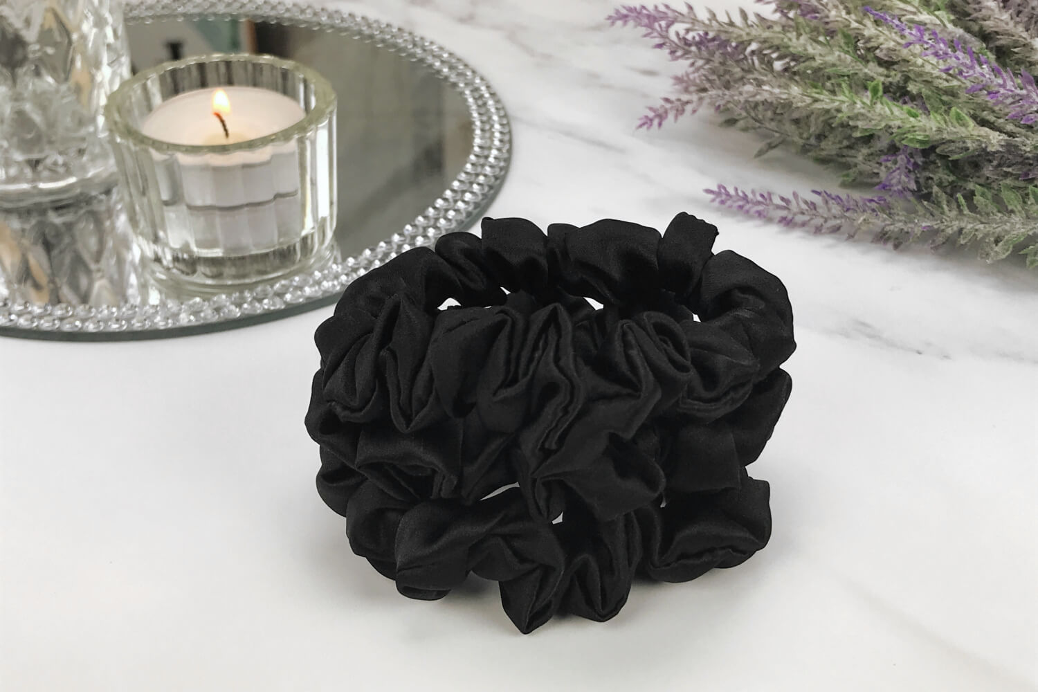 Celestial Silk skinny black silk scrunchies stacked on marble counter with lavender plant and a candle in the background