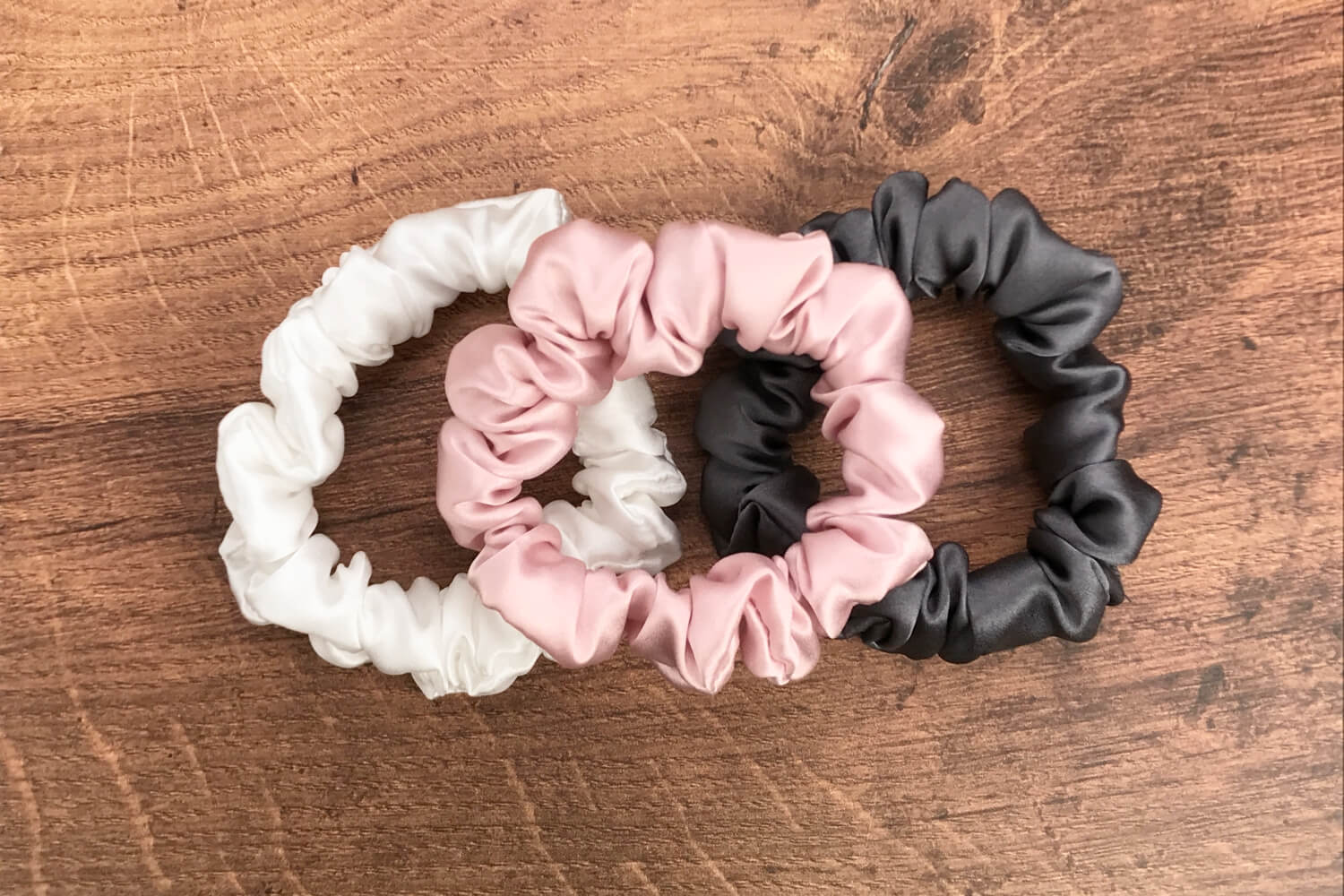 thin charcoal ivory and pink silk hair ties by Celestial Silk laying in a pile on a wood vanity