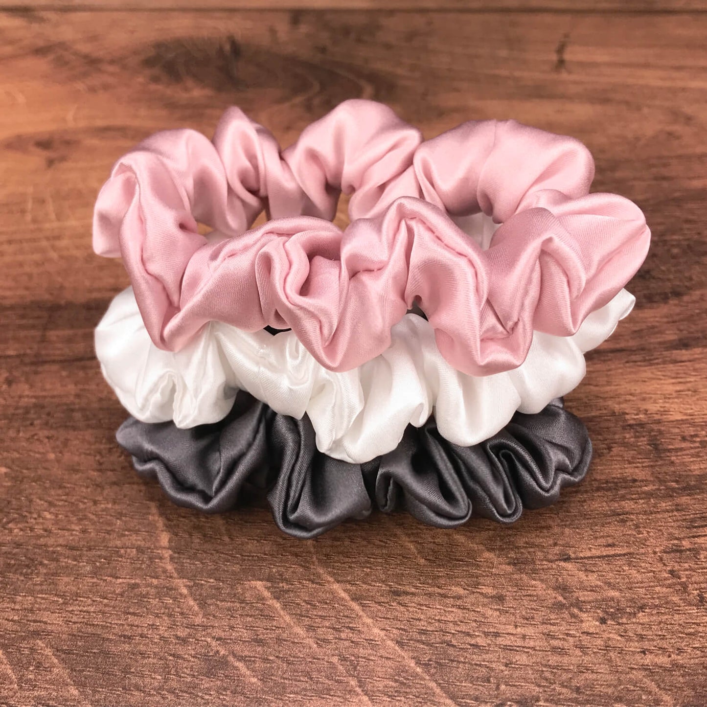thin charcoal ivory and pink silk hair ties by Celestial Silk stacked in a pile on a wood vanity