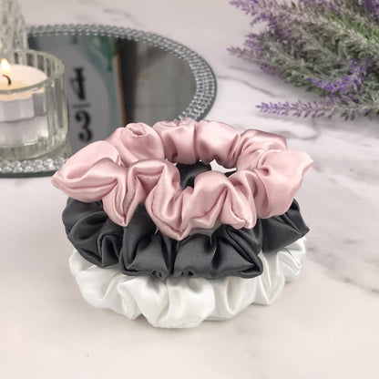 Celestial Silk skinny charcoal ivory and pink silk scrunchies stacked on marble counter with lavender plant and a candle in the background