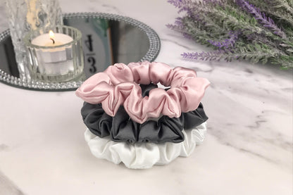 Celestial Silk skinny charcoal ivory and pink silk scrunchies stacked on marble counter with lavender plant and a candle in the background