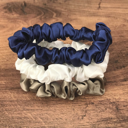 thin dark taupe navy and ivory silk hair ties by Celestial Silk stacked in a pile on a wood vanity