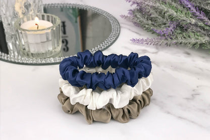 Celestial Silk skinny dark taupe navy and ivory silk scrunchies stacked on marble counter with lavender plant and a candle in the background
