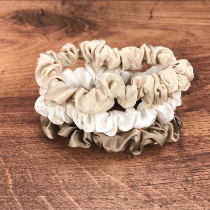 thin dark taupe ivory and taupe silk hair ties by Celestial Silk stacked in a pile on a wood vanity