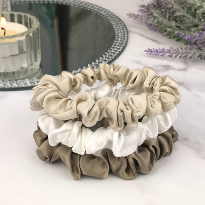 Celestial Silk skinny dark taupe ivory and taupe silk scrunchies stacked on marble counter with lavender plant and a candle in the background