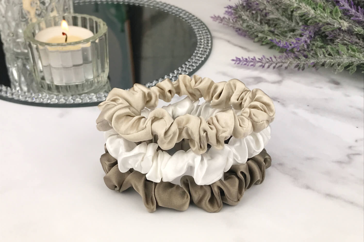 Celestial Silk skinny dark taupe ivory and taupe silk scrunchies stacked on marble counter with lavender plant and a candle in the background