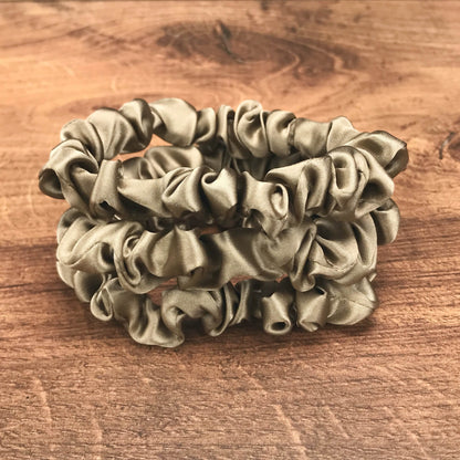 thin dark taupe silk hair ties by Celestial Silk stacked in a pile on a wood vanity
