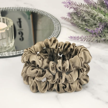 Celestial Silk skinny dark taupe silk scrunchies stacked on marble counter with lavender plant and a candle in the background