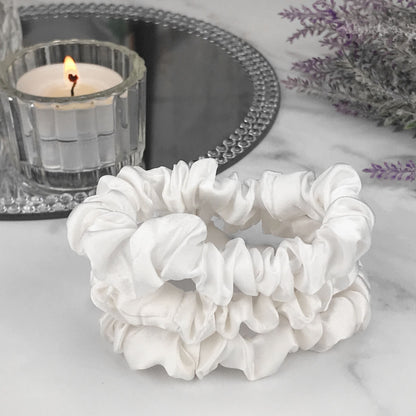 Celestial Silk skinny ivory silk scrunchies stacked on marble counter with lavender plant and a candle in the background