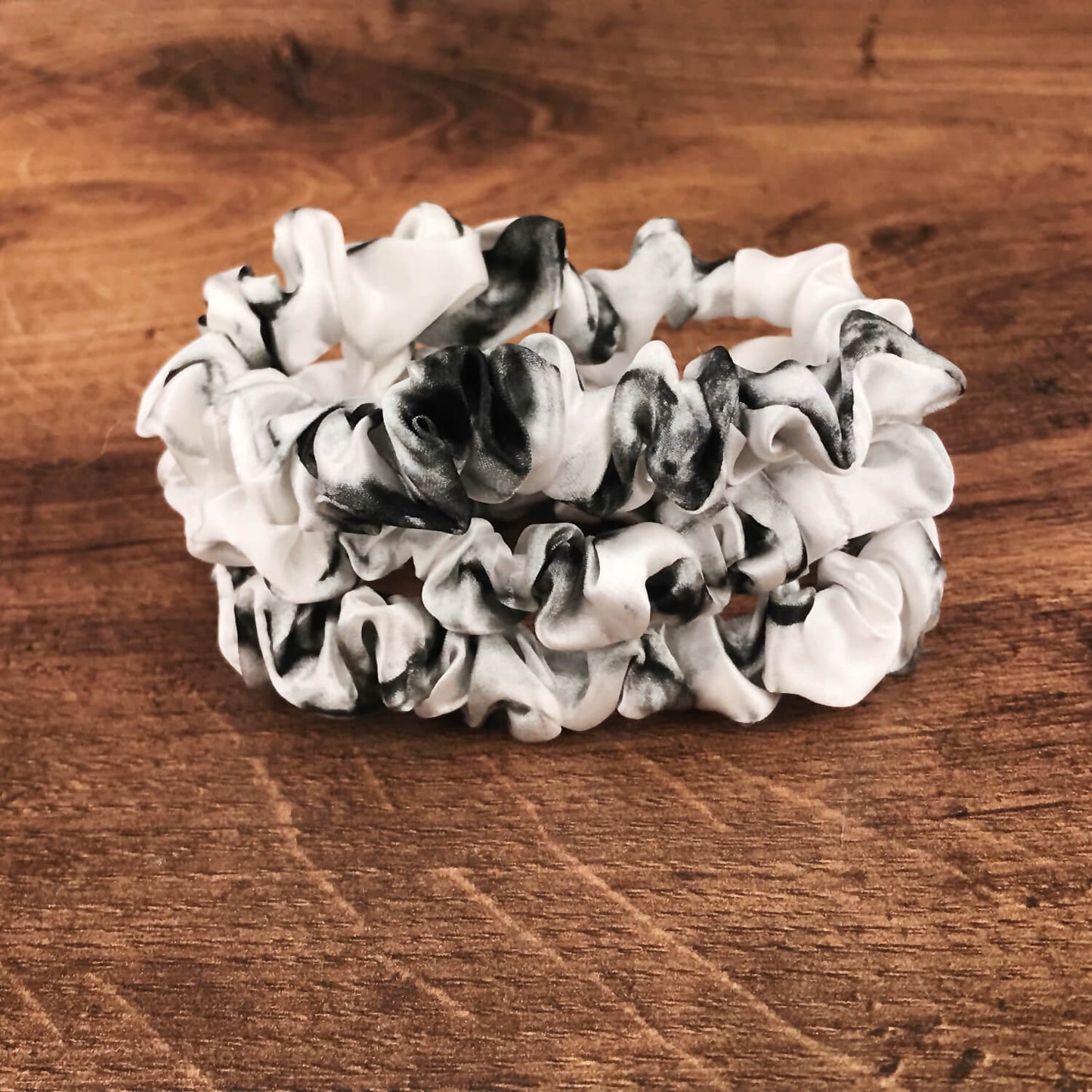 thin white marble silk hair ties by Celestial Silk stacked in a pile on a wood vanity