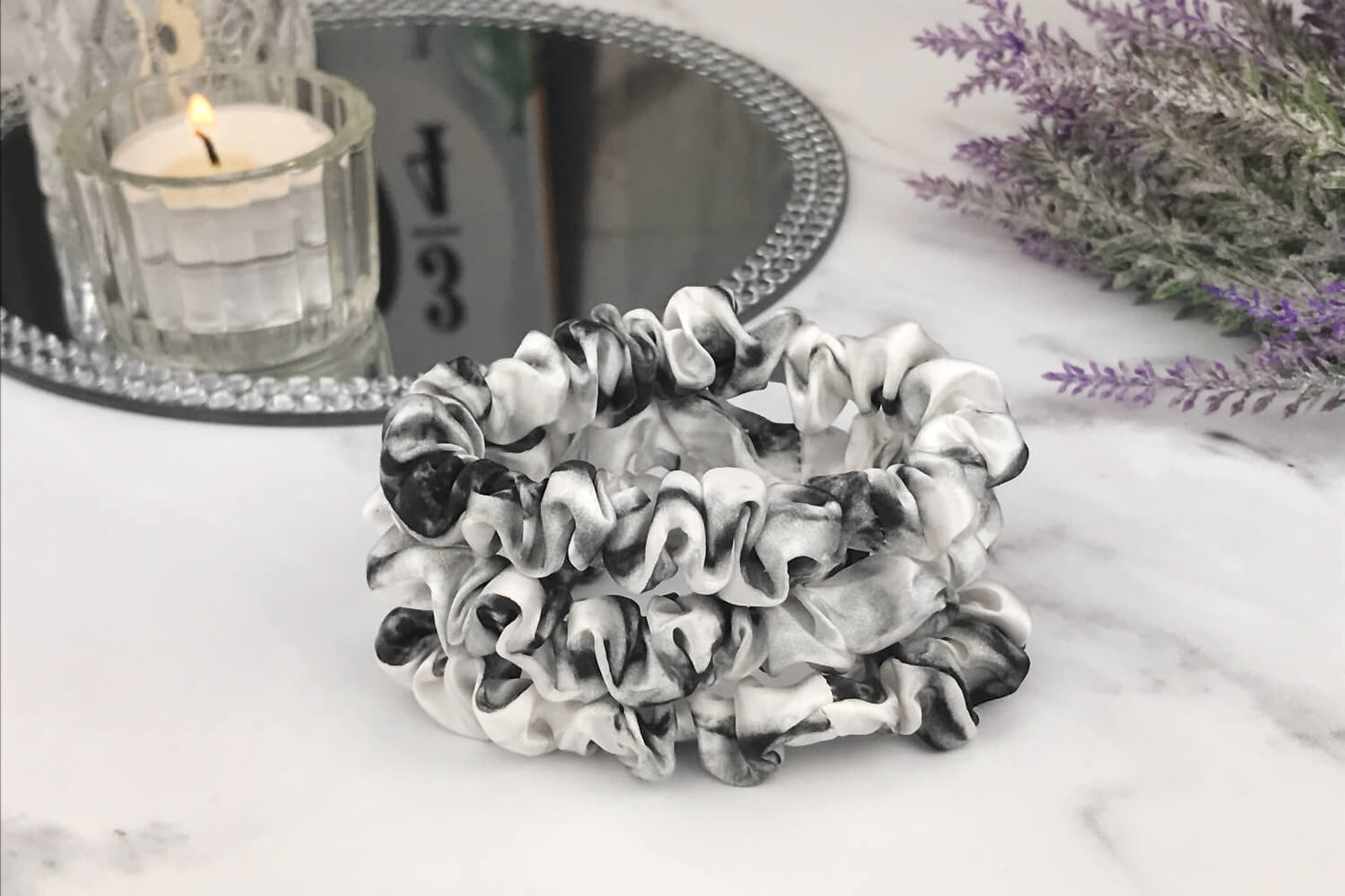 Celestial Silk skinny white marble silk scrunchies stacked on marble counter with lavender plant and a candle in the background